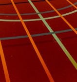 A sports court with intersecting lines in orange and blue, creating geometric patterns on a reddish-brown surface.